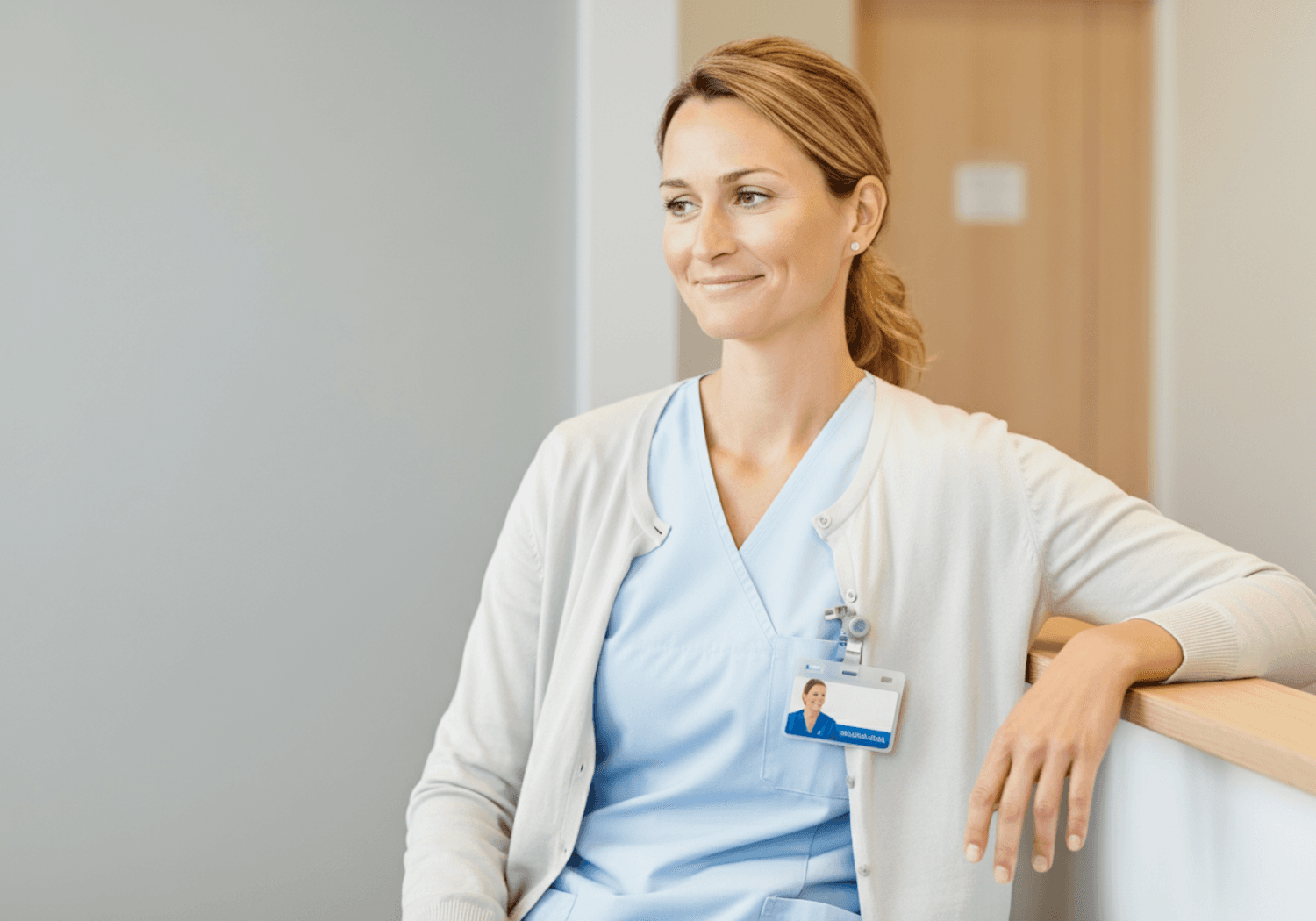 Portrait of a nurse in light blue scrubs and a white cardigan, smiling softly